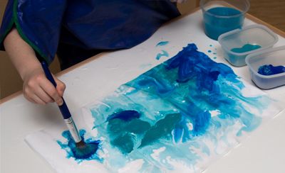 A child applying paint to a piece of paper with a thick paintbrush