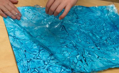 A child’s hands peeling a layer of cling film off a piece of paper
