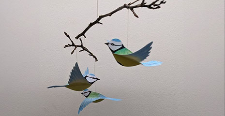 three paper blue tits hanging from branches