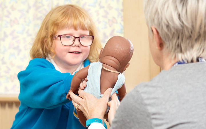 Child handing doll to teacher