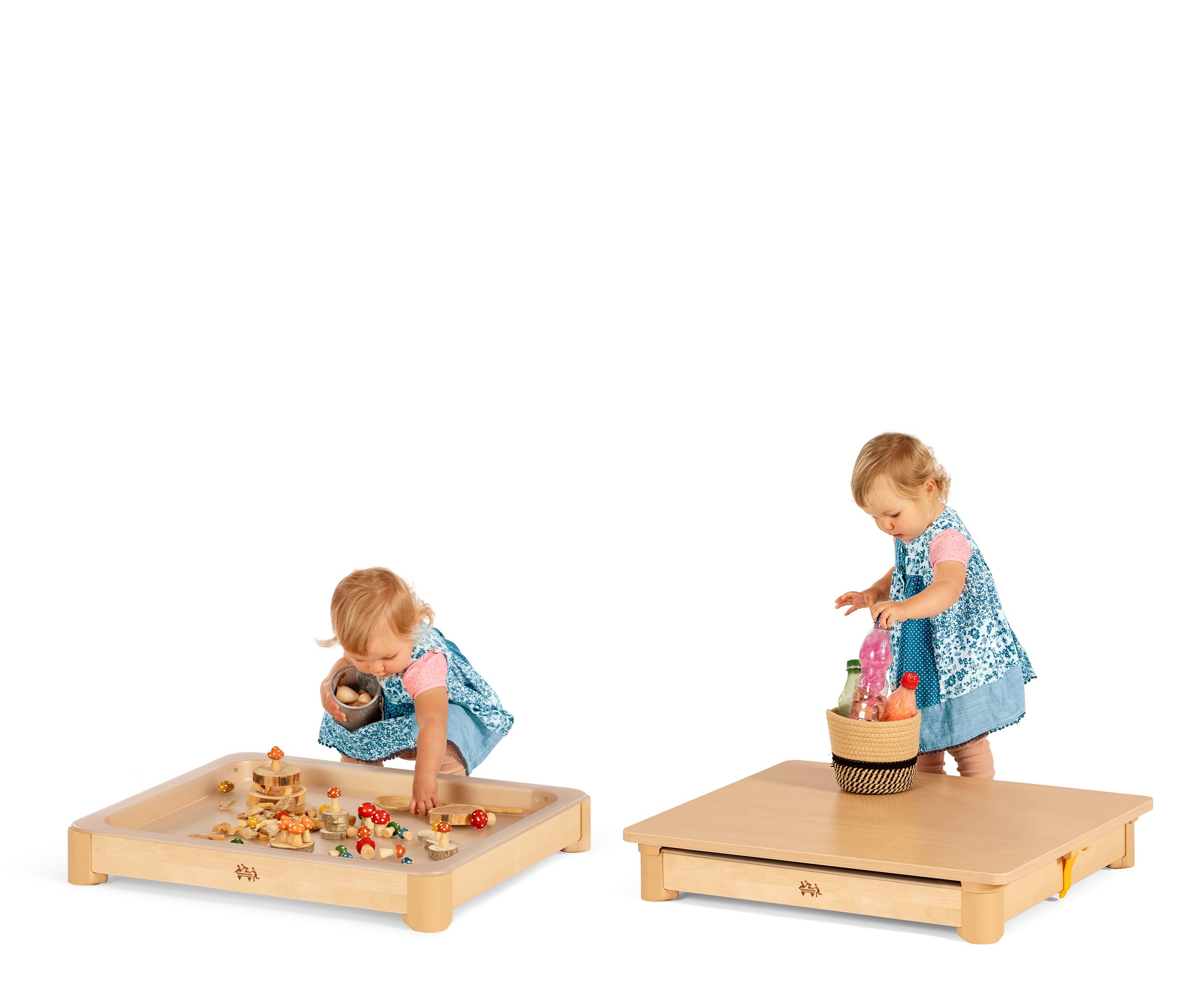 A baby girl in a blue patchwork dress playing with sensory materials in the Activity floor tray.