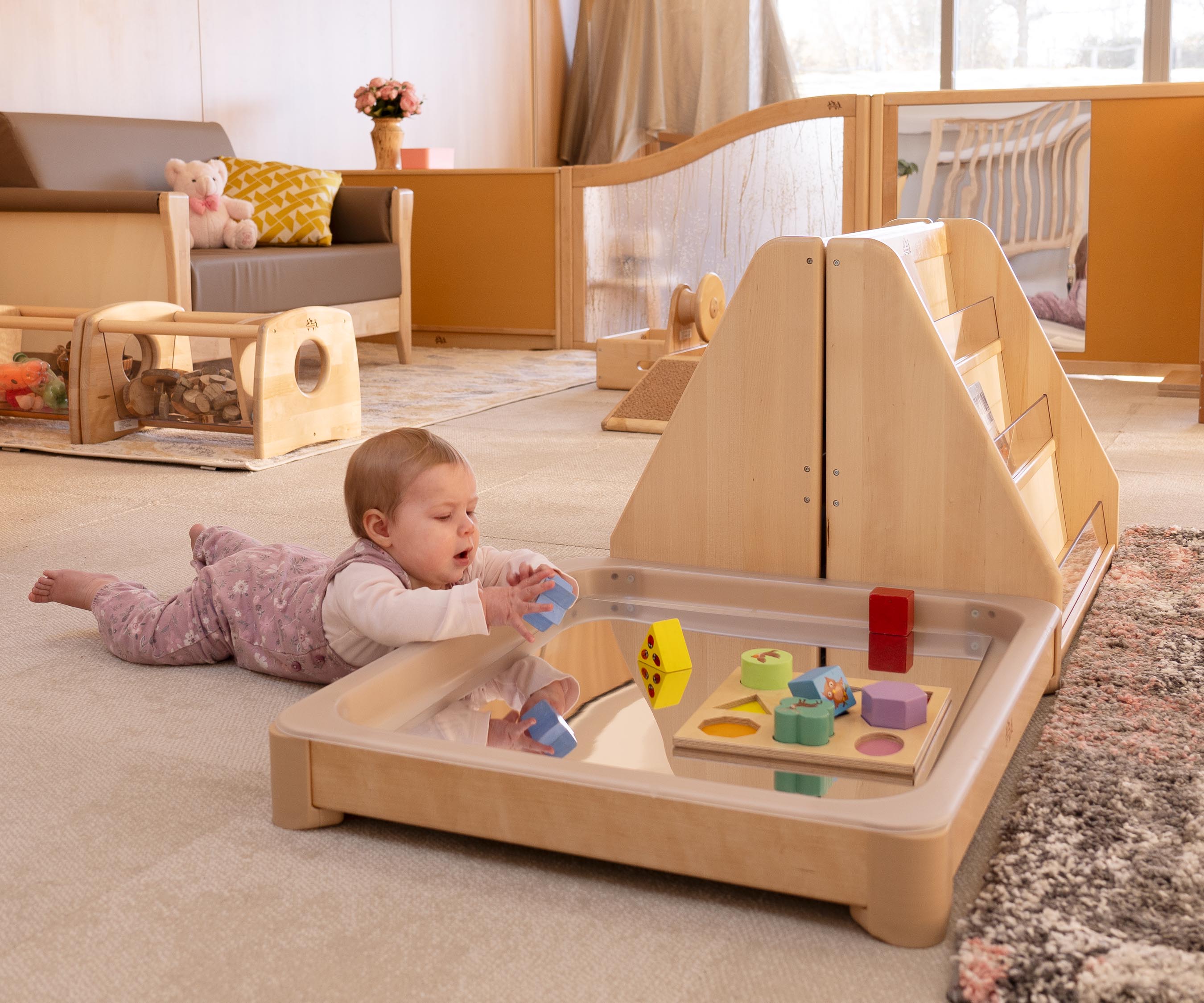 Baby girl in lavender romper playing with a wooden puzzle in an Activity floor tray, a tuff tray alternative that allows even small children to reach the centre.