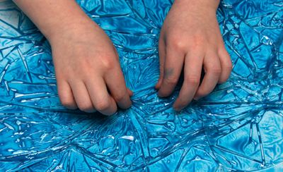 A child’s hands pulling up cling film on a piece of paper with wet paint