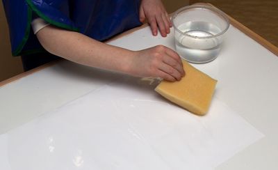 A child wetting a sheet of paper with a sponge