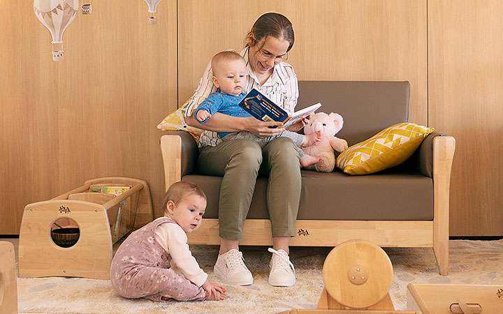 A teacher and baby reading a book together on a Nursery sofa in a baby room designed with calming natural colours 