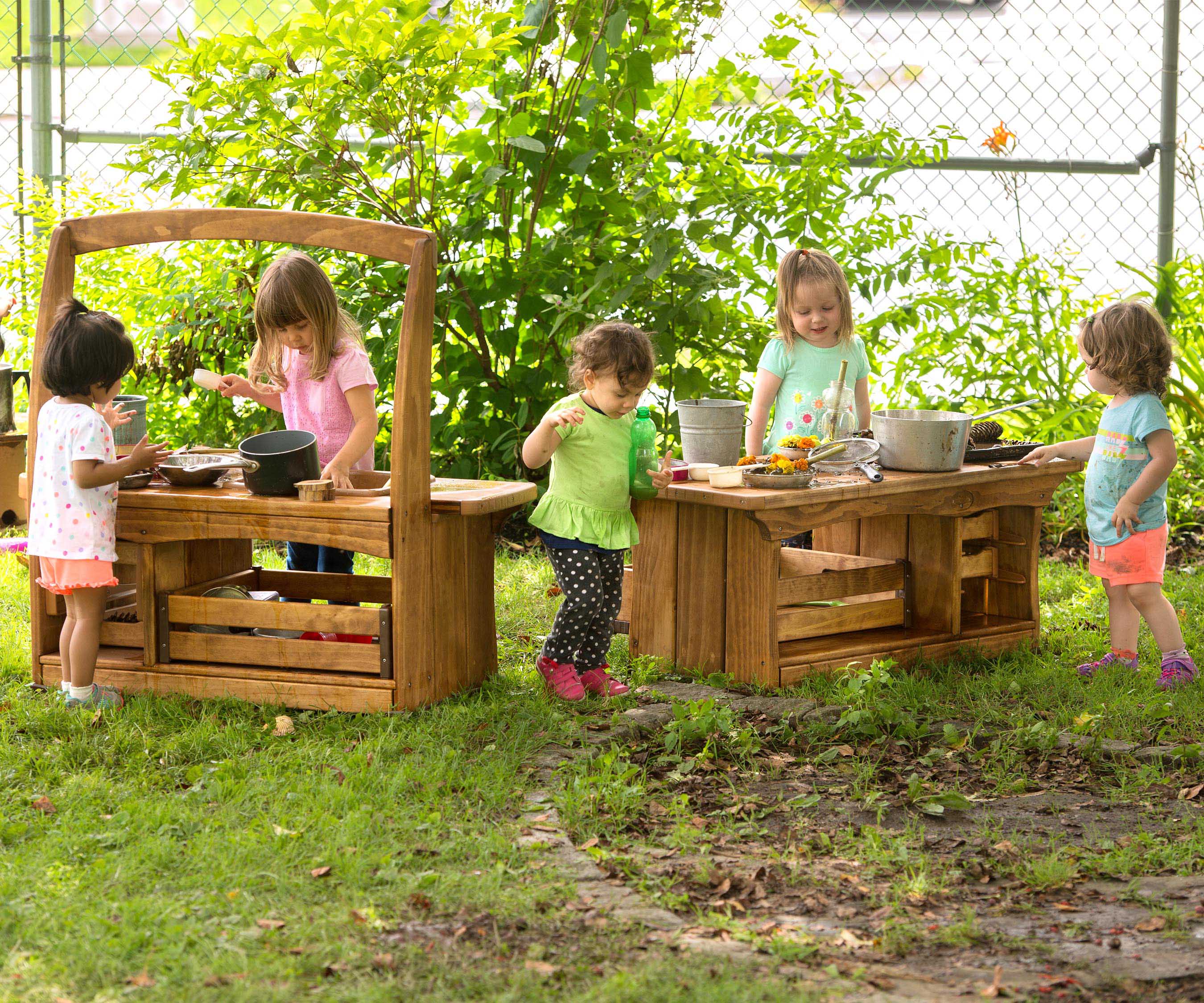 Children play with natural materials in an outdoor play area created with a toddler mud kitchen sink and counter.