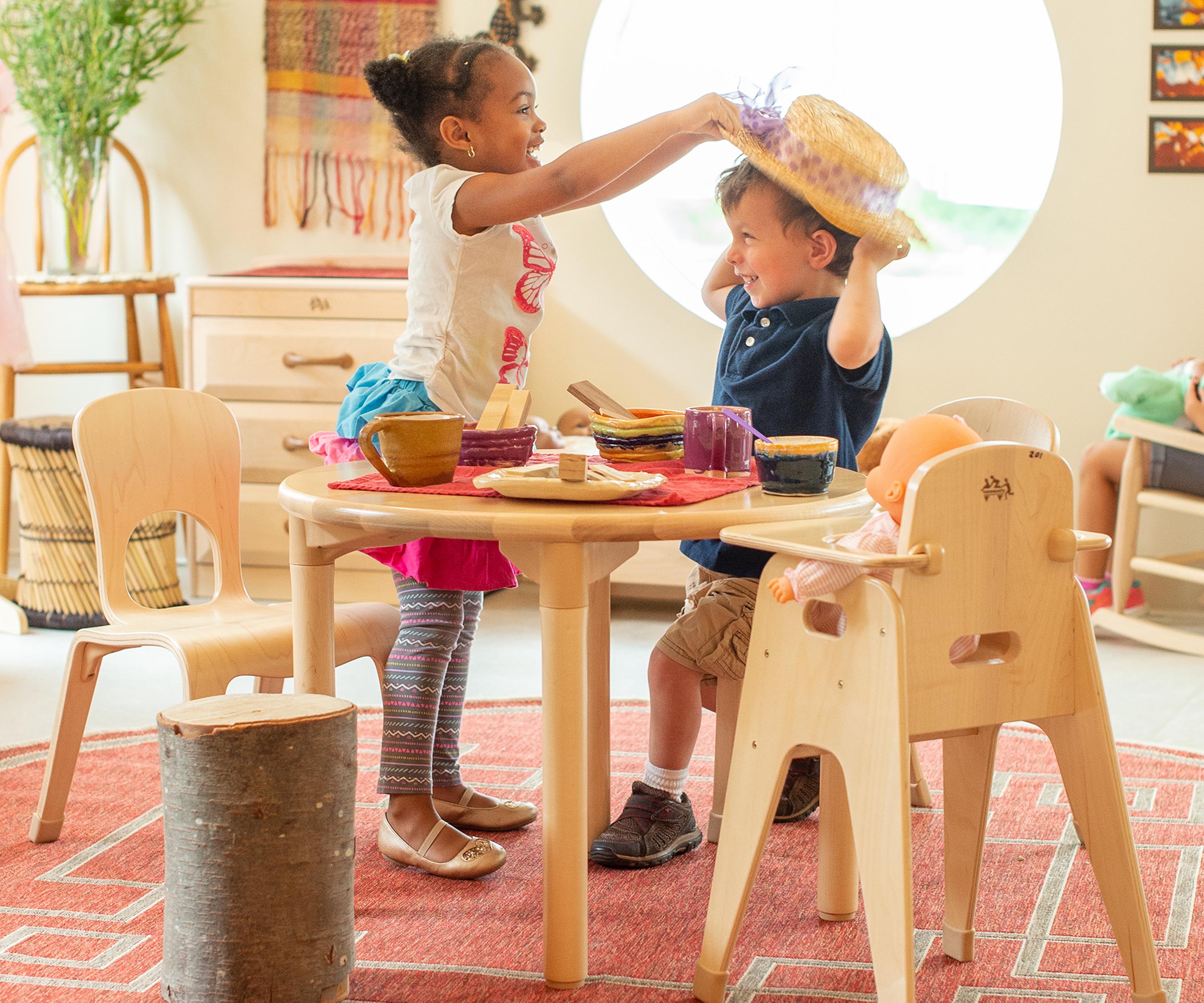 A boy and girl at a solid wood table in the home corner 